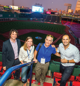 Three men and women stand in front of the Fenway grounds at night